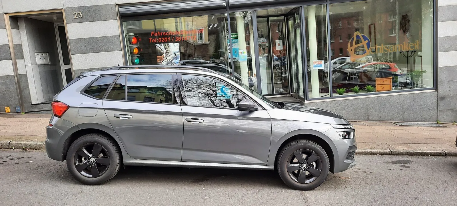 Straßenansicht der Fahrschule Steinhoff: Schaufenster mit Aufkleber „Fahrschule Steinhoff Tel. 0201/3614712“, davor der graue Skoda Kamiq, links die Hausnummer 23